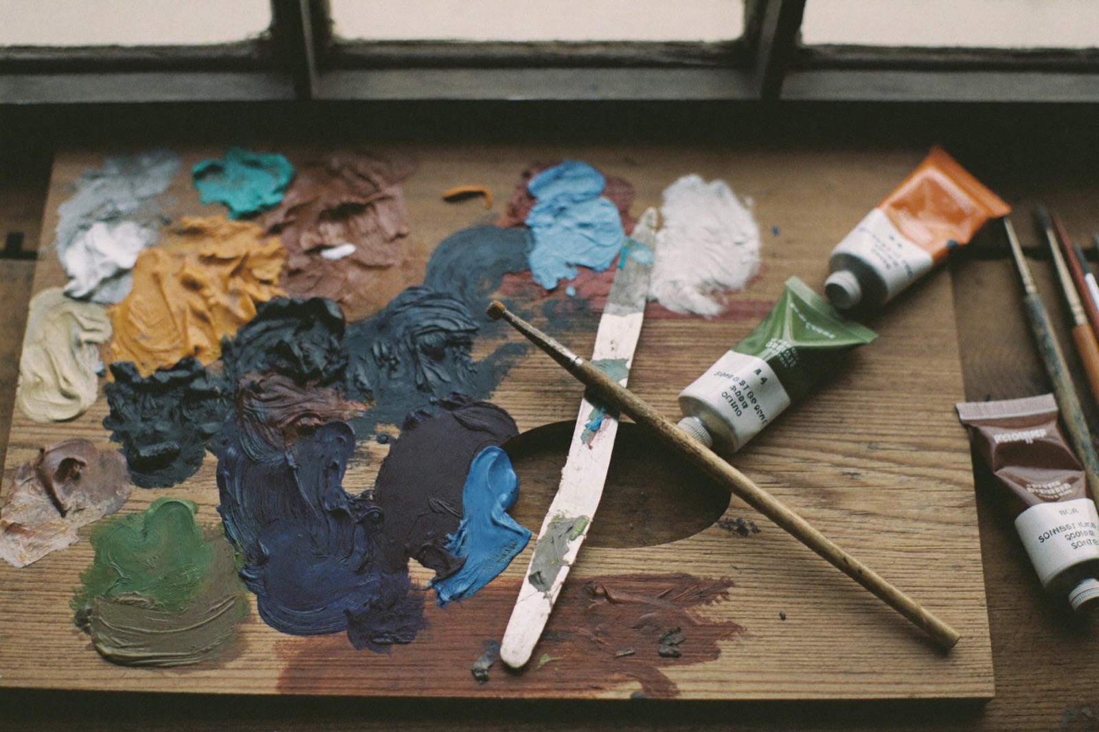 Well-used wooden palette with oils in blues, teals and ochres, brushes and palette knife